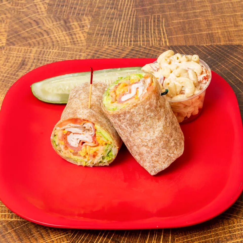Two wraps with meat, cheese, and lettuce, a pickle spear, and macaroni salad on a red plate.