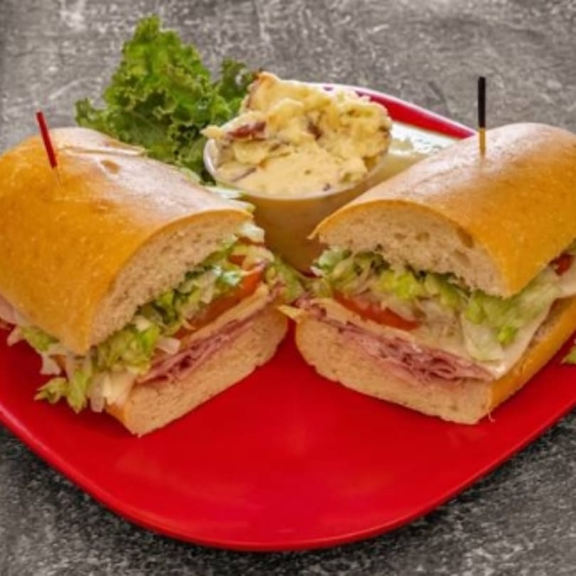A sliced sub sandwich with meat, cheese, lettuce, and tomato, served with potato salad and lettuce.