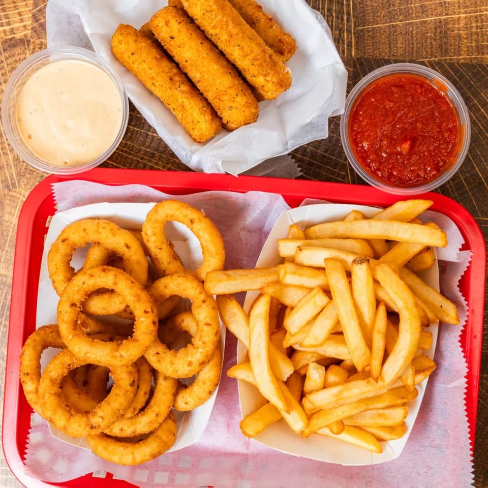 A red tray with onion rings and french fries, mozzarella sticks, and two dipping sauces.
