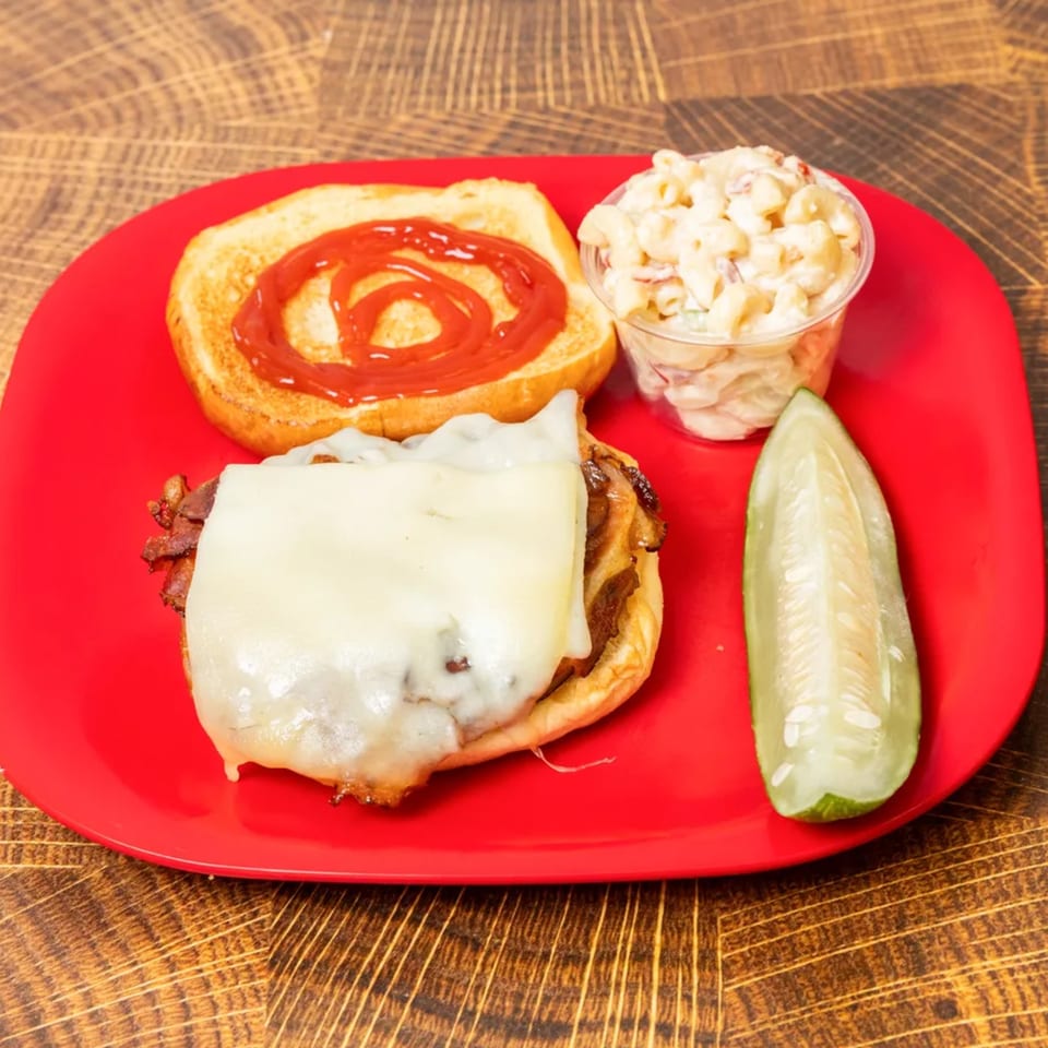 Cheesesteak sandwich with macaroni salad and a pickle spear on a red plate.
